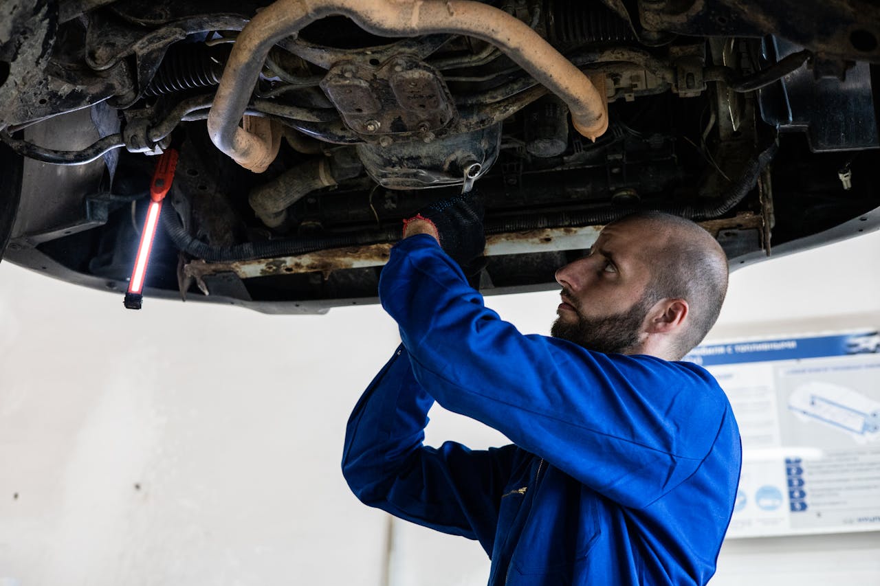 Mechanic in blue coveralls works under a car, focusing on repairs in a garage setting.
